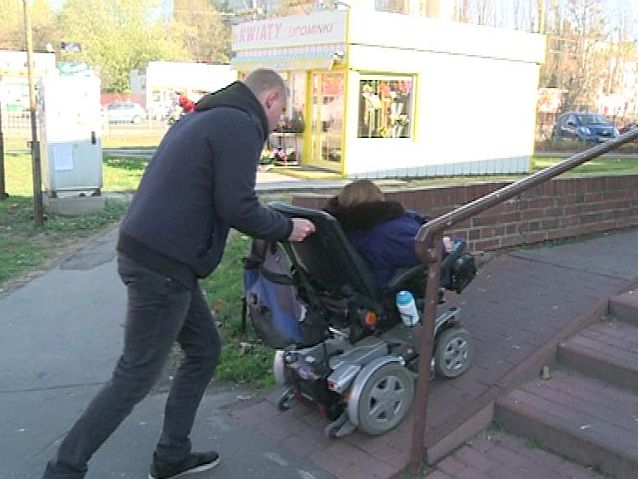 mężczyzna - asystent pomaga kobietę na wózku wjechać po podjeździe