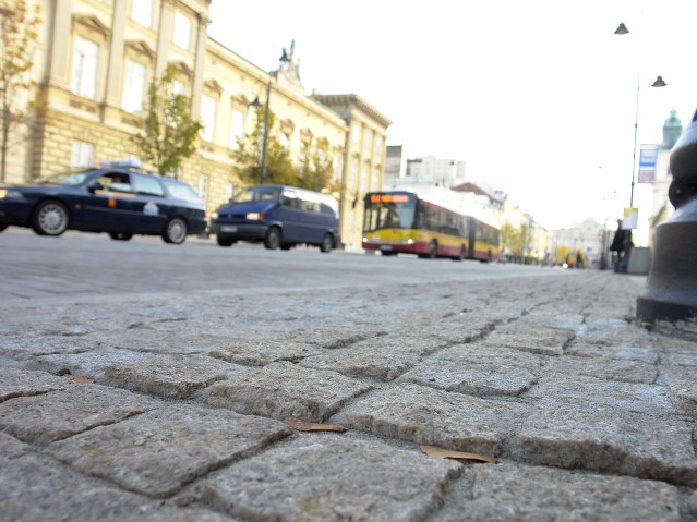 wyboista kostka na chodniku, obok jadący autobus miejski