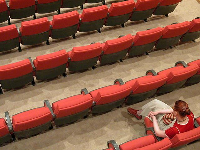 Puste krzesła na sali kinowej. Na jednym z nich siedzi samotna pani