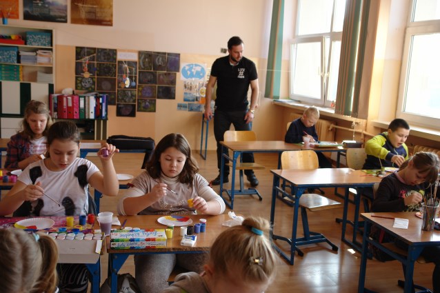 asystent patrzący na pracę dziecka, podczas malowania w klasie