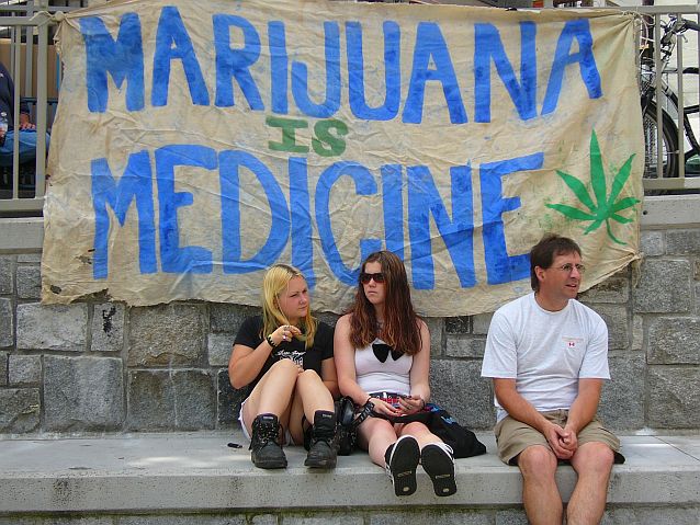 Dwie kobiety i mężczyzna siedzą pod transparentem z napisem: Marijuana is medicine