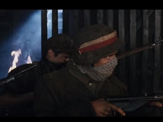 kadr z filmu Miasto44, dwóch powstańców idzie z bronią, mają zasłonięte twarze, by nie wdychać dymu i ognia