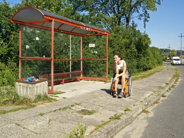 dziewczyna na wózku czeka na autobus na przystanku w mniejszej miejscowości