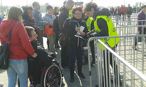 Widzowie, w tym mężczyzna na wózku, przed wejściem na stadion