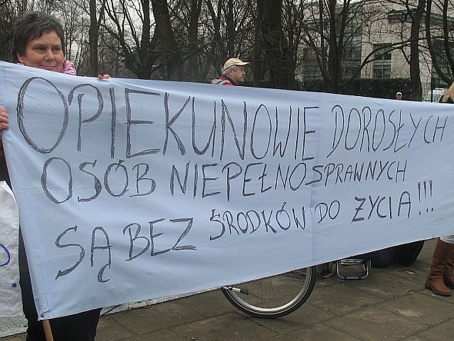 Protest. Transparent: "Opiekunowie dorosłych osób niepełnosprawnych są bez środków do życia!!!"