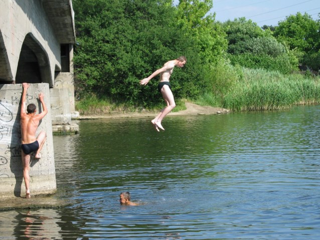 chłopak skacze z mostu do wody, inny wspina się na most