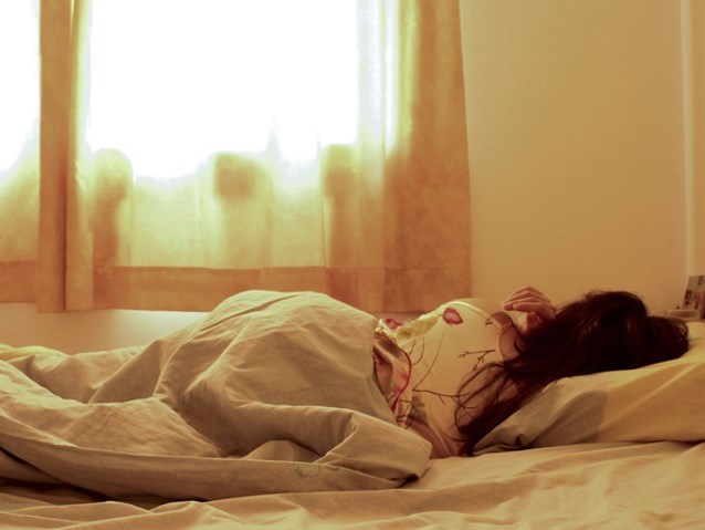 kobieta leży tyłem na łóżku, przykryta pościelą