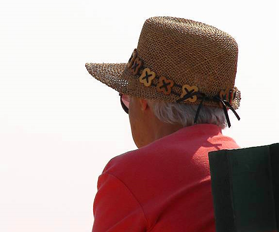 Starsza kobieta w kapeluszu siedzi odwrócona tyłem