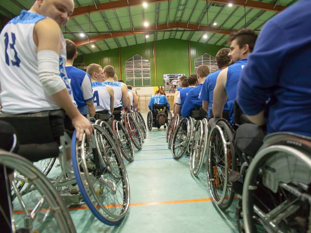 dwa obok siebie rzędy zawodników na wózkach w niebieskich koszulkach