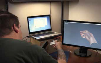 mężczyzna z nakładką na przedramieniu, imitującą prawdziwą rękę na ekranie komputera