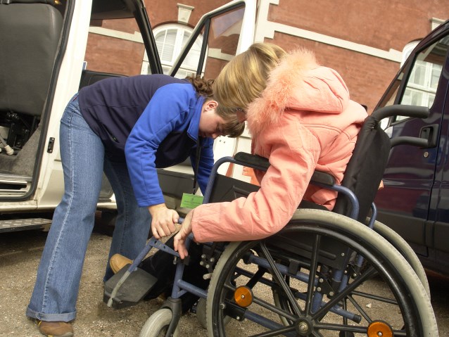 asystentka osoby z niepełnosprawnością pomaga zamocować paski w wózku tuż przed wejściem do specjalistycznego transportu
