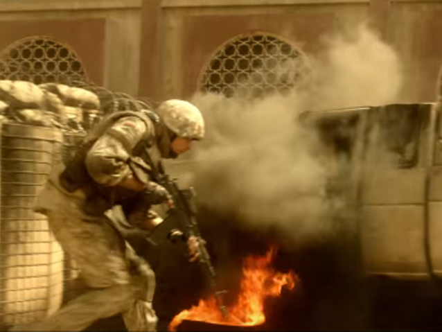 schylony w pół żołnierz biegnie przy palącym się samochodzie