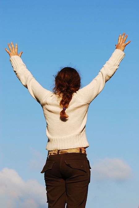 Kobieta stojąc trzyma ręce w górze, wyciągnięte do nieba