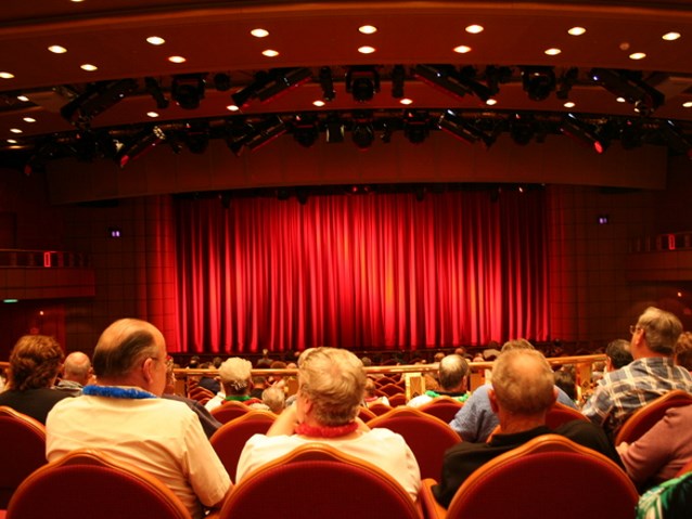 publiczność siedząca w teatrze, w tle czerwona kurtyna
