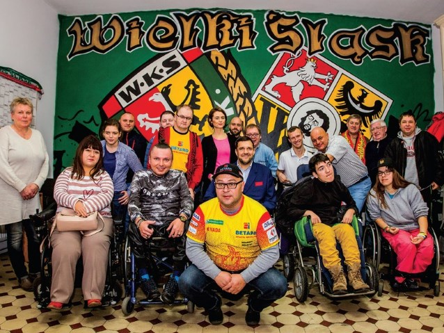 kilka osób na wózkach inwalidzkich razem z osobami pełnosprawnymi na tle napisu WKS Wielki Śląsk