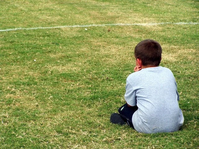 chłopiec siedzi sam na trawie