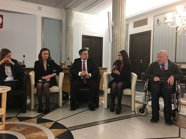 Paneliści siedzą w półkolu podczas konferencji w eleganckiej sali