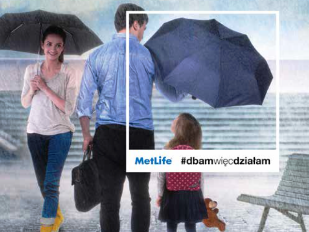 mężczyzna trzyma parasol nad małą córką z plecakiem. Obok nich przechodzi uśmiechnięta młoda kobieta z parasolem