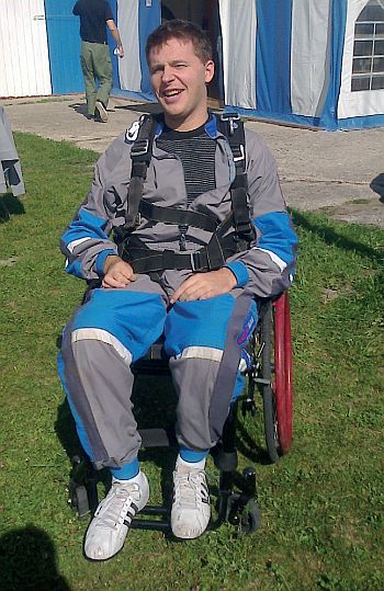 Uśmiechnięty Mateusz Puszkarski na wózku i w uprzęży skoczka spadochronowego