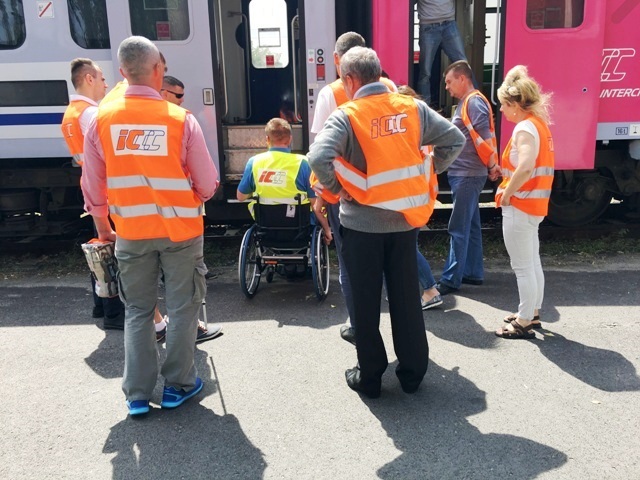 kilku pracowników PKP Intercirty stoi na peronie tuż obok trenera, który jest na wózku. Naprzeciw nich znajduje się pociąg i trzy schodki