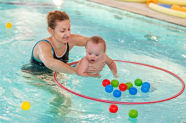 Basen. Kobieta trzyma małe dziecko w wodzie, wokół dziecka kolorowe piłeczki i hula hop