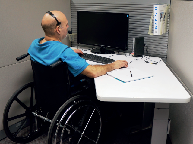 mężczyzna siedzi na wózku przy biurku i pracuje przed laptopem