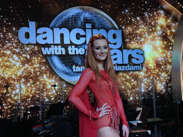 Iwona Cichosz w stroju tancerki stoi na tle napisu Dancing with the Stars. Taniec z Gwiazdami