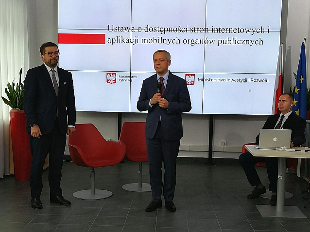 Minister stoi i mówi do mikrofonu, obok dwaj mężczyźni, z tyłu napis: Ustawa o dostępności stron internetowych i aplikacji mobilnych organów publicznych