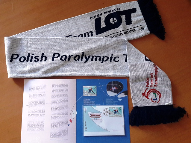 Na biurku leży szalik i znaczek pocztowy wraz z kopertą Zimowych Igrzysk Paraolimpijskich w Pjongczangu