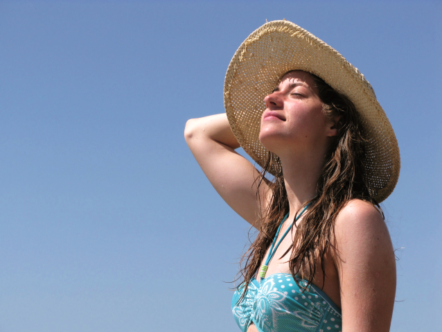 Dziewczyna w niebieskim stroju kąpielowym ze słomkowym kapeluszem wystawia twarz do słońca