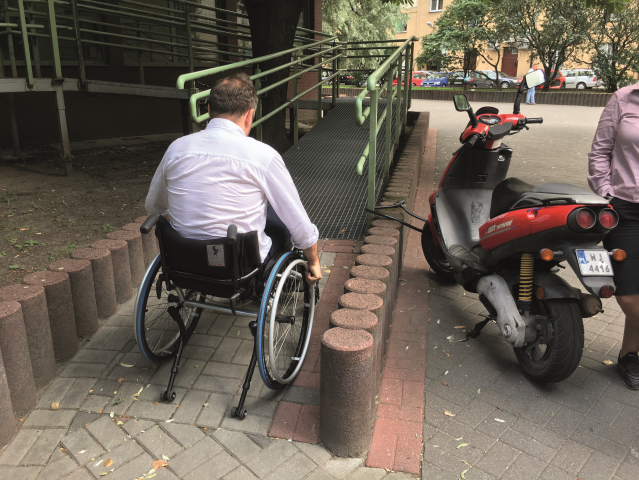 mężczyzna na wózku wjeżdża po długim podjeździe do budynku