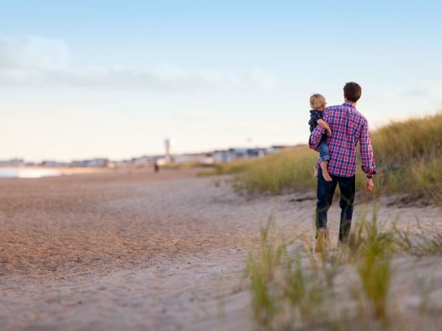 ojciec trzyma na ręku dziecko widoczni od tyłu spacerują po plaży