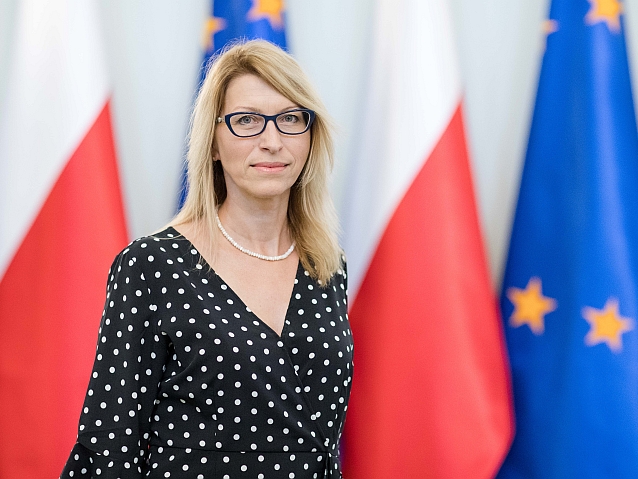 Paulina Malinowska-Kowalczyk stoi na tle flag polskich i Unii Europejskiej.