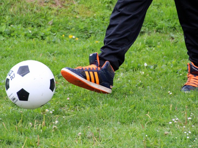 widoczne nogi chłopca kopiące na trawie piłkę
