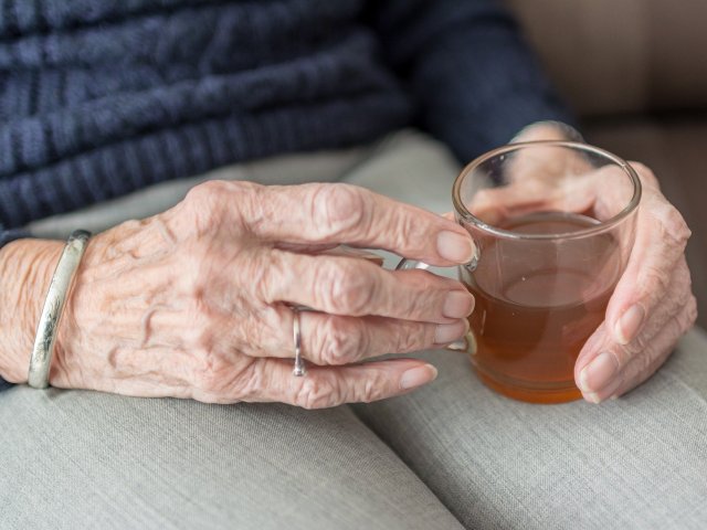 ręce starszej kobiety trzymają szklanke z herbatą