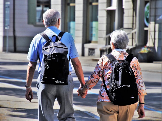 starszy mężczyzna i kobieta idą widziani od tyłu, trzymają się za ręce