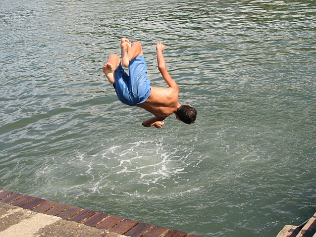 Kręcąc salto w powietrzu młody chłopak skacze do wody z nabrzeża