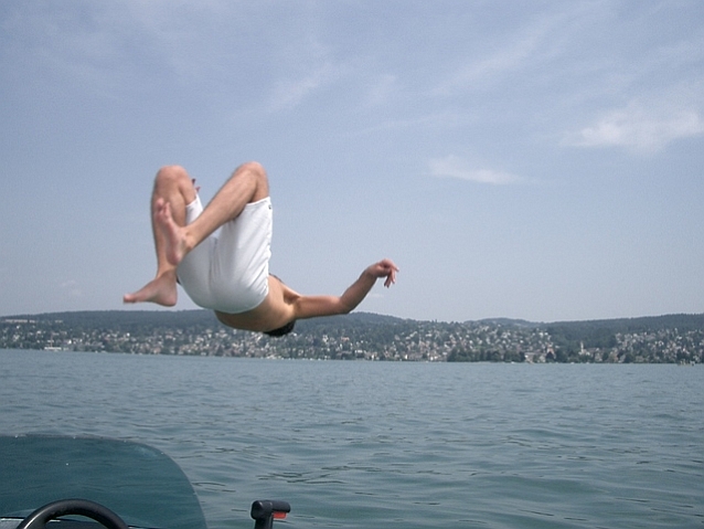 Mężczyzna skacze z motorówki do wody, do której tafli jest odwrócony plecami