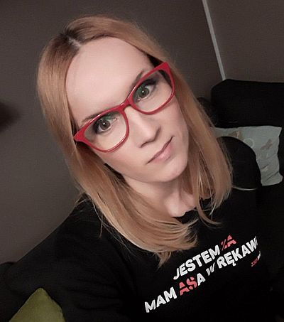 Izabela Hnidziuk-Machnica - młoda kobieta w czerwonych okularach i czarnej koszulce z napisem: jestem ZA, mam ASa w rękawie