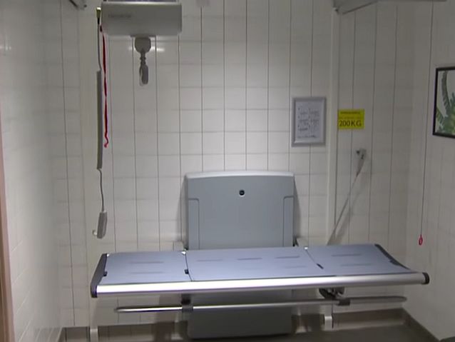 Wnętrze łazienki. Stojąca pod ścianą stabilna kozetka, a nad nią elektryczny podnośnik do przenoszenia osoby z niepełnosprawnością
