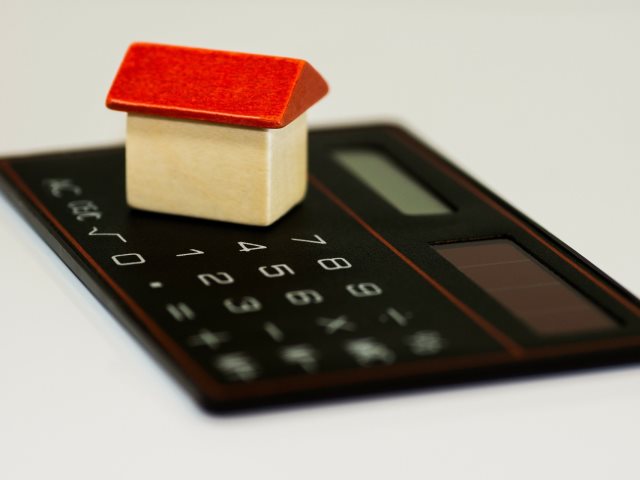 mały drewniany domek z czerwonym dachem stoi na kalkulatorze