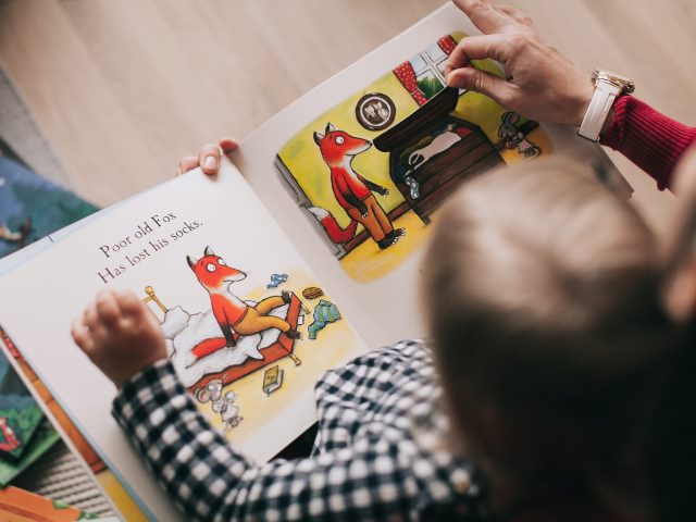 z góry małe dziecko przegląda obrazkową książkę ręka dorosłego odkrywa obrazek