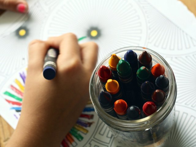 ręka dziecka trzyma kredkę i rysuje obok stoi słoik z kredkami