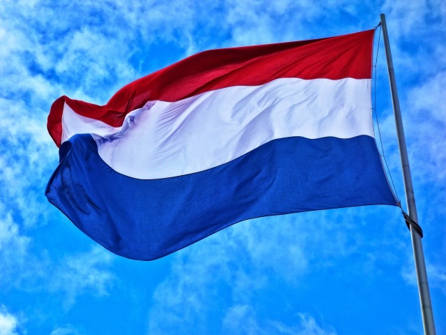 na tle nieba powiewa flaga holenderska czerwono biało niebieska