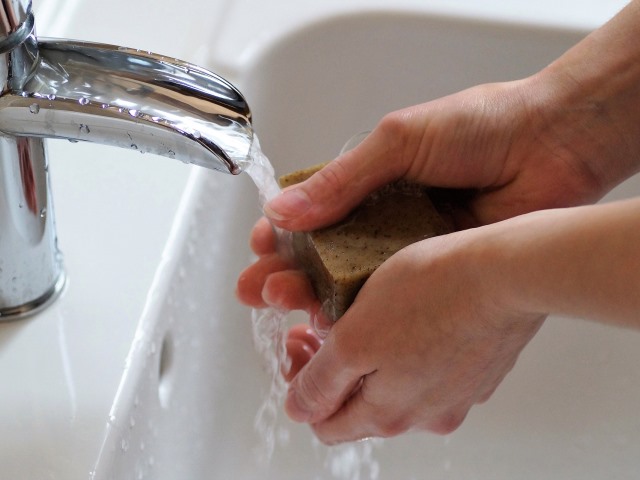 kobieta myje ręce mydłem z kranu leci woda, widać tylko jej dłonie
