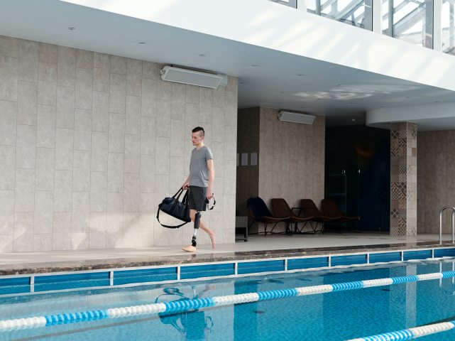 młody mężczyzna idzie brzegiem basenu na protezie jednej nogi
