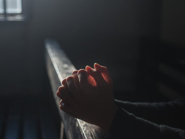 w ciemności ręce złożone do modlitwy oparte o ławkę