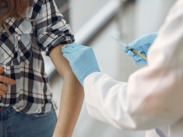 ręka kobiety z powiniętym rękawem i rękę medyka w rękawiczce trzymającą strzykawkę do szczepienia