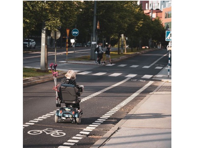 kobieta na wózku elektrycznym jedzie ścieżką rowerową za wózkiem ma zatknięte kule