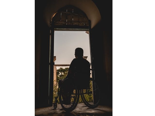 meżczyzna na wózku stoi tyłem w otwartych drzwiach na balkon